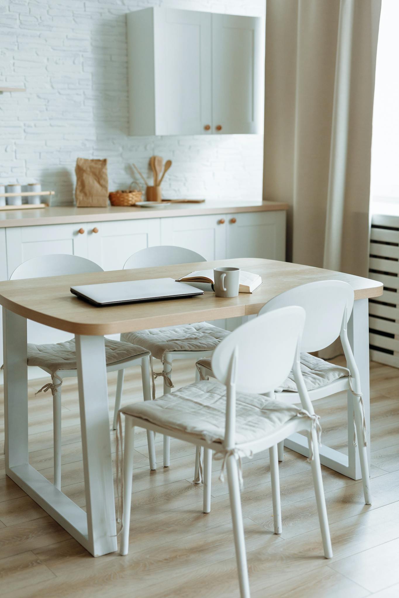 Bright minimalist kitchen setup with dining table, laptop, and mug.