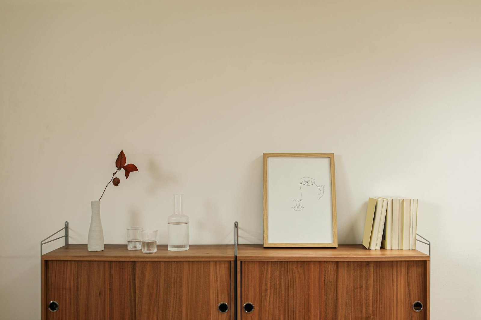 Elegant minimalist interior featuring a wooden cabinet with books, ceramics, and simple art