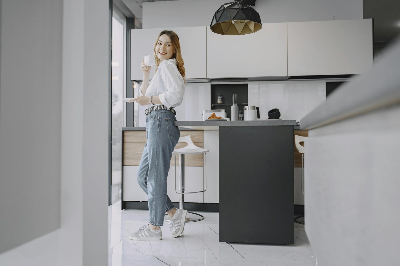 Woman in casual attire enjoying a hot beverage in a stylish, modern kitchen.